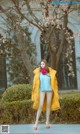 A woman in a yellow coat is posing for a picture.