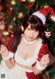 A woman in a santa claus outfit posing in front of a Christmas tree.