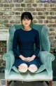 A woman sitting in a blue chair in front of a brick wall.