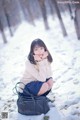 A woman sitting in the snow with a handbag.