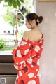 A woman in a red kimono leaning against a wall.