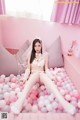 A woman in a white lingerie sitting on a bed of pink and white balls.